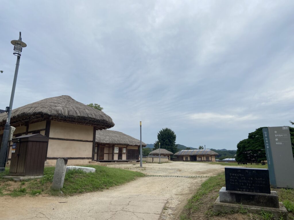 Traditional thatched-roof houses in Hahoe Folk Village, Andong, South Korea, under a cloudy summer sky.