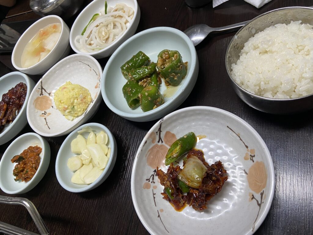 韓国の焼肉店で提供されるパンチャンと呼ばれるおかずと白米。丸い小皿に、ニンニク、青唐辛子の和え物、サラダなどがそれぞれ小皿に入っている。