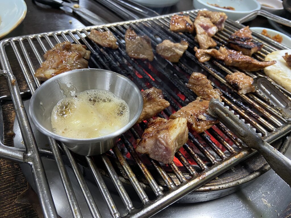 網の上で焼かれているデジカルビの横に置かれた、ごま油入りの銀色のアルミカップ。