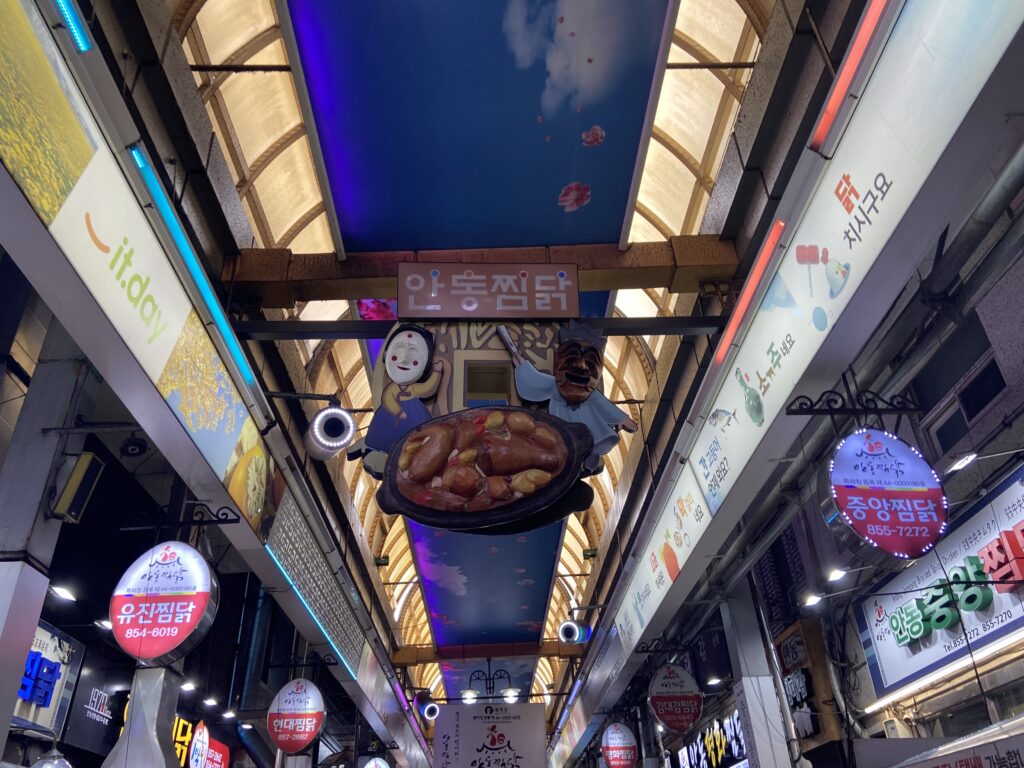 Interior of Andong’s Chimdak Street, with hanging decorations featuring Andong Jjimdak dishes and traditional mask motifs suspended from the ceiling.