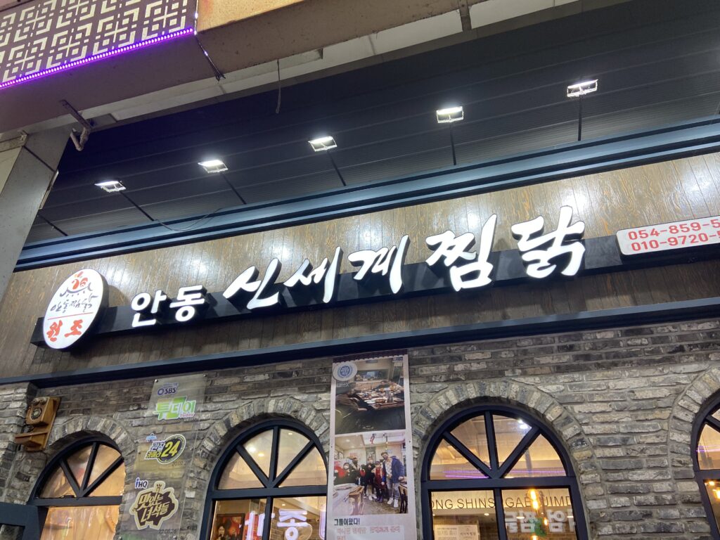 新世界チムタクの店舗外観。レンガ造りの外壁と、昼目立つ白い大きな店名の文字。