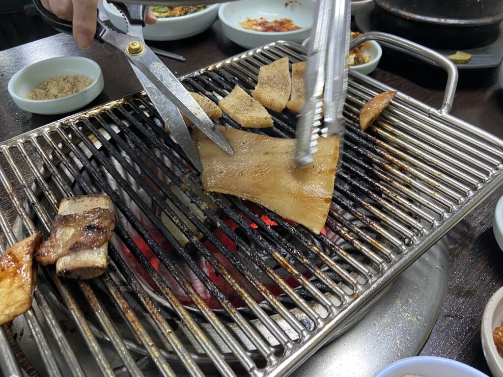 プイルスップルカルビでお肉を食べた後にサービスとして提供されるデジコプテギ（豚の皮）。炭火の上で焼かれており、ハサミでカットしている様子。