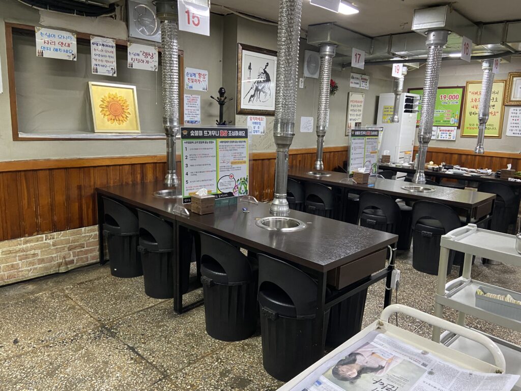 韓国・ヨンドゥンポの焼肉店、プイルスップルカルビの店内。炭火焼き用のテーブル席が並び、席ごとに換気ダクトが設置されている。