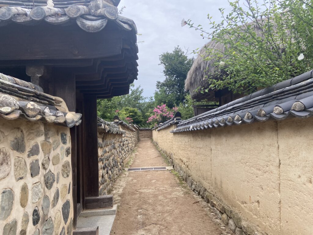 韓国の伝統的な家屋が建ち並ぶ、河回村の狭い散策路。右側は土壁、左側は石垣で、奥には別の建物が見える。