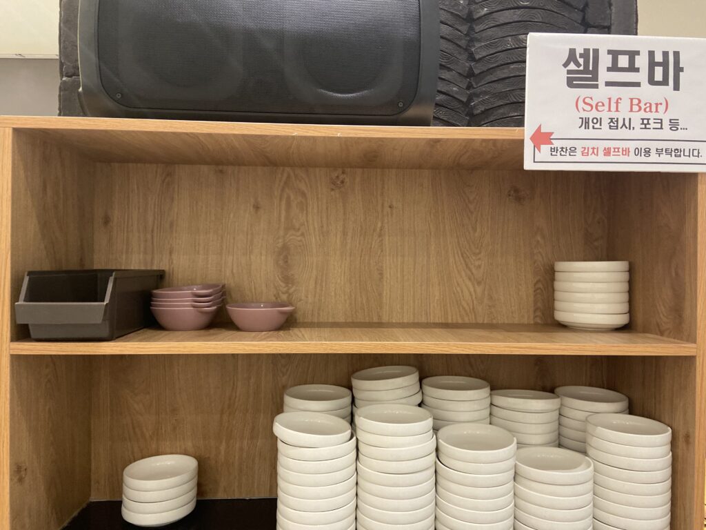 Self-service bar at Hwangsaengga Kalguksu, with plates, forks, and kimchi available for customers to serve themselves.