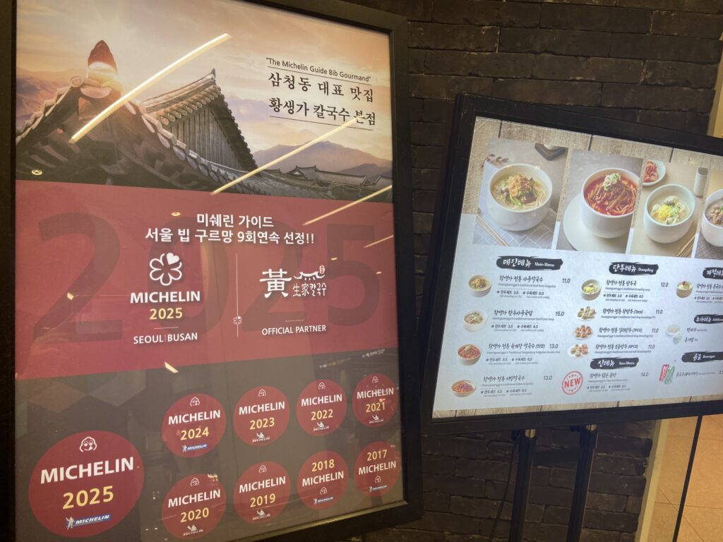 Michelin Guide poster on the left and menu board on the right at Hwangsaengga Kalguksu branch.