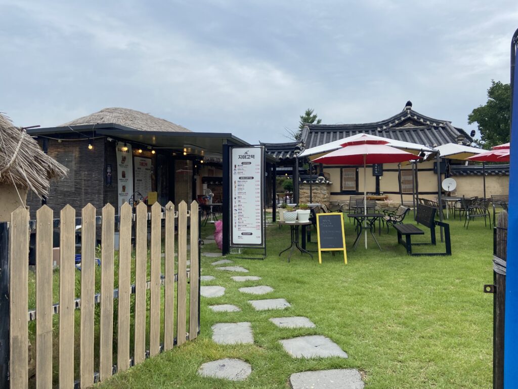 An outdoor café in Hahoe Folk Village with traditional Korean-style buildings, red-and-white umbrellas, and neatly arranged tables on a grassy lawn.