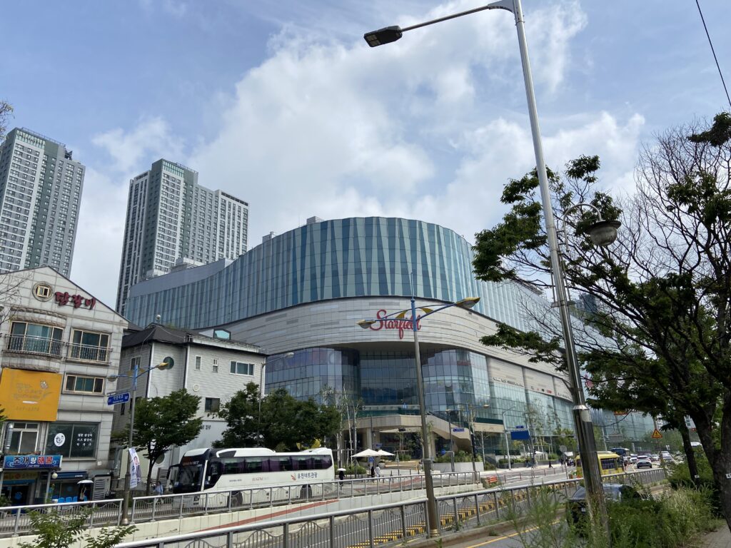 ガラス面のモダンな外観のスターフィールドスウォンのショッピングモール。建物手前にはバスが停車しており、背景には高層アパート群がそびえている。