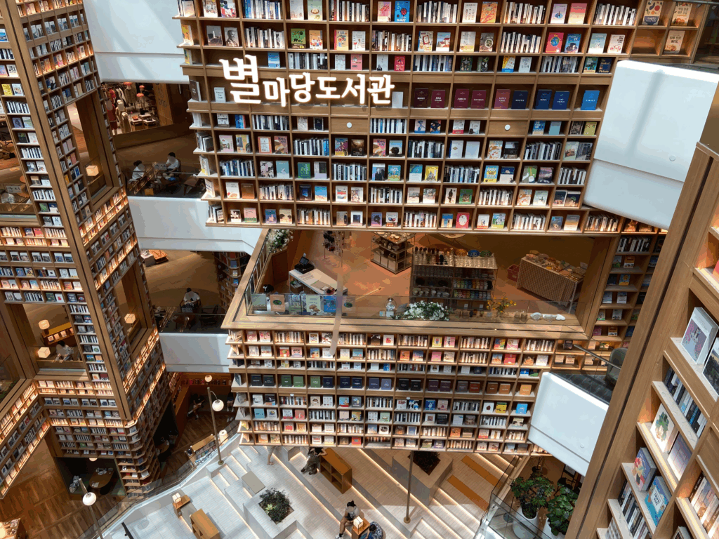 スターフィールドスウォンのピョルマダン図書館の壮大な空間。何層にも連なる巨大な本棚が壁を覆い、中央にはハングルでピョルマダン図書館の文字が記されている。白い階段状の休憩スペースや、張り出したテラス席で人々が静かに本を読んだりくつろいだりしている様子。