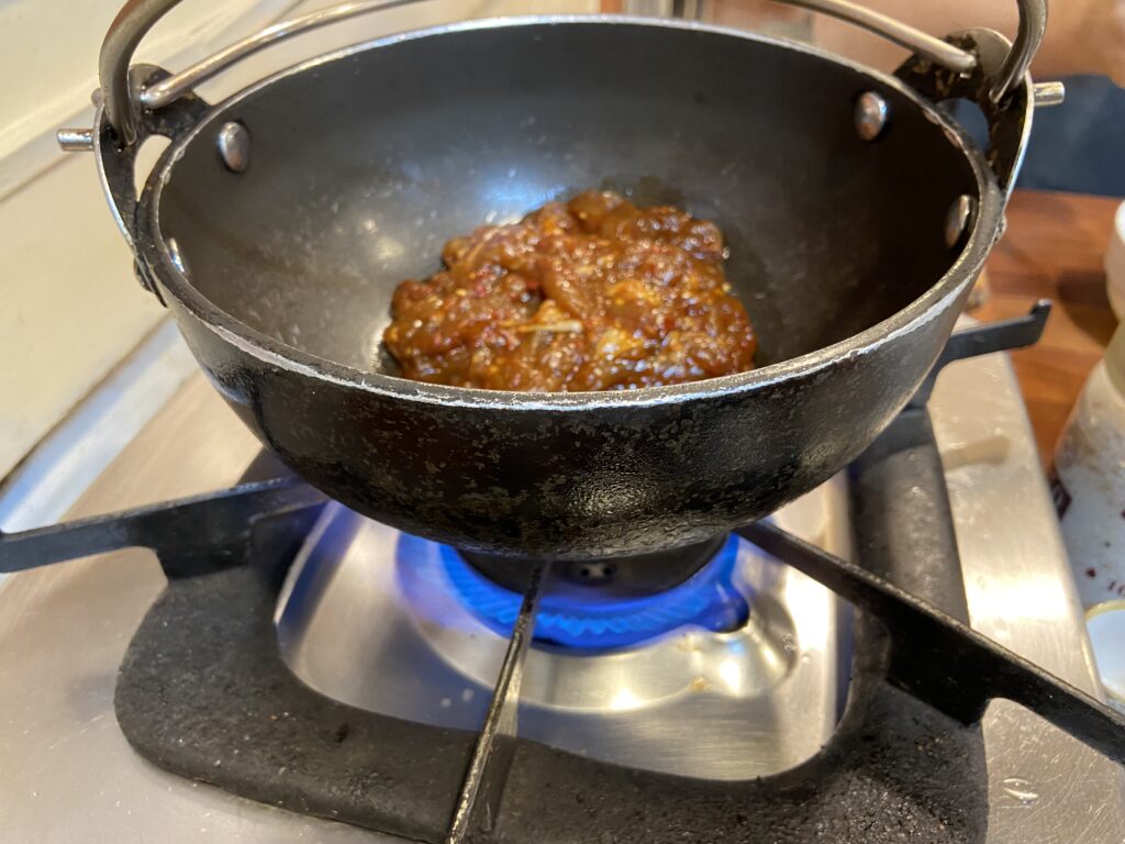 Marinated spicy Chicken Bulgogi being cooked in a black pot on a tabletop gas stove.