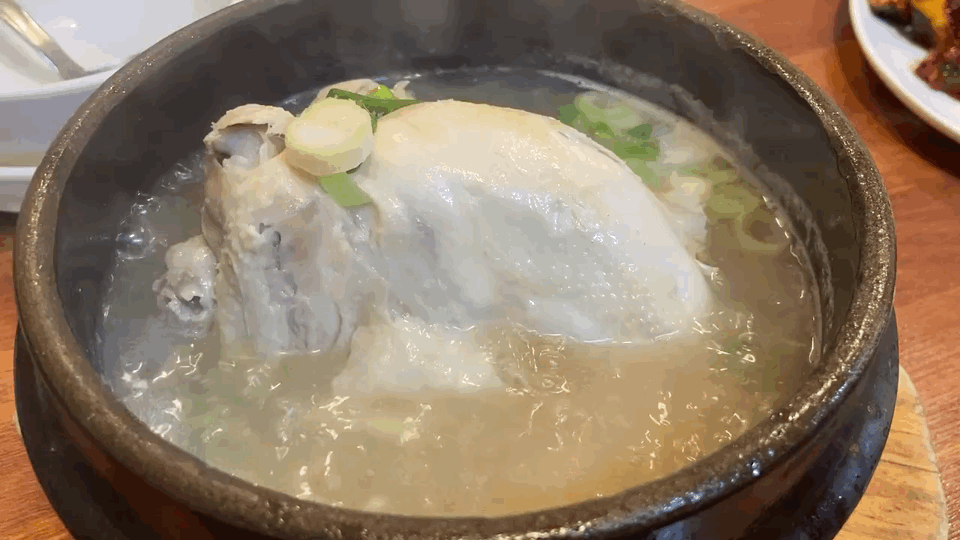 黒い鍋の中でグツグツと煮え立つ、熱々のサムゲタン。丸ごとの鶏肉と白濁したスープに、刻んだネギが乗っている。