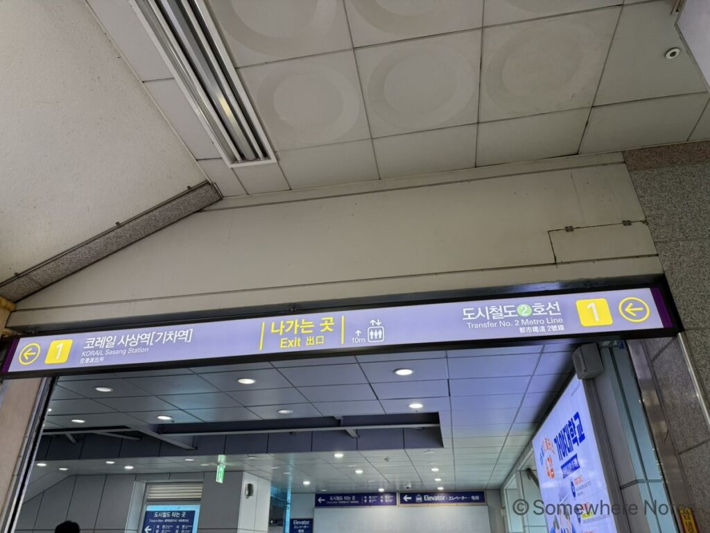 沙上（ササン）駅構内の頭上案内板。都市鉄道（地下鉄）2号線への乗り換えを示す、緑色の「2」のマークと矢印が表記されています。