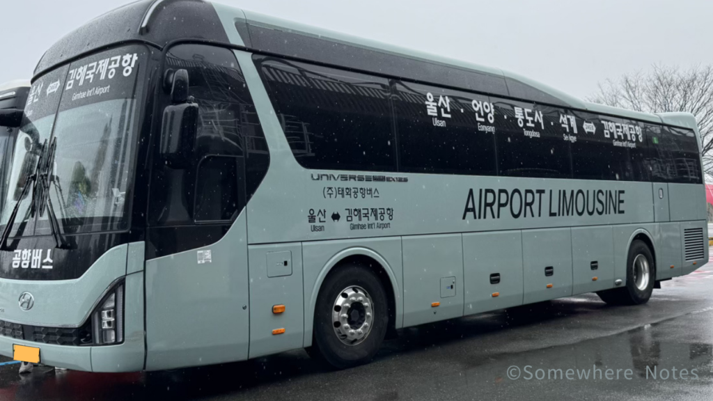雨が降る中、屋外に停車している薄水色の空港リムジンバス。車体側面には大きく「AIRPORT LIMOUSINE」と印字されている。